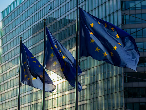 EU flags waving in front of a glass building at sunrise