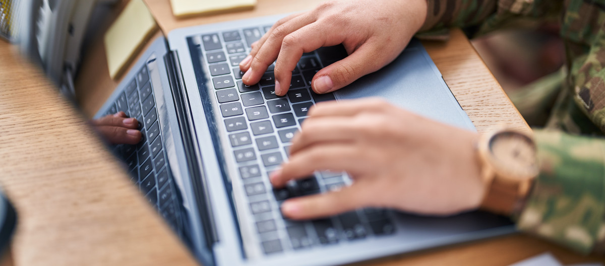Hands on a laptop keyboard, person is wearing camouflage