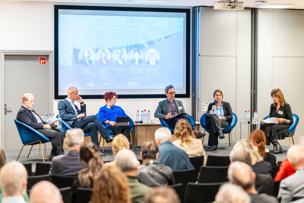 Six people discussing on a stage in front of an audience