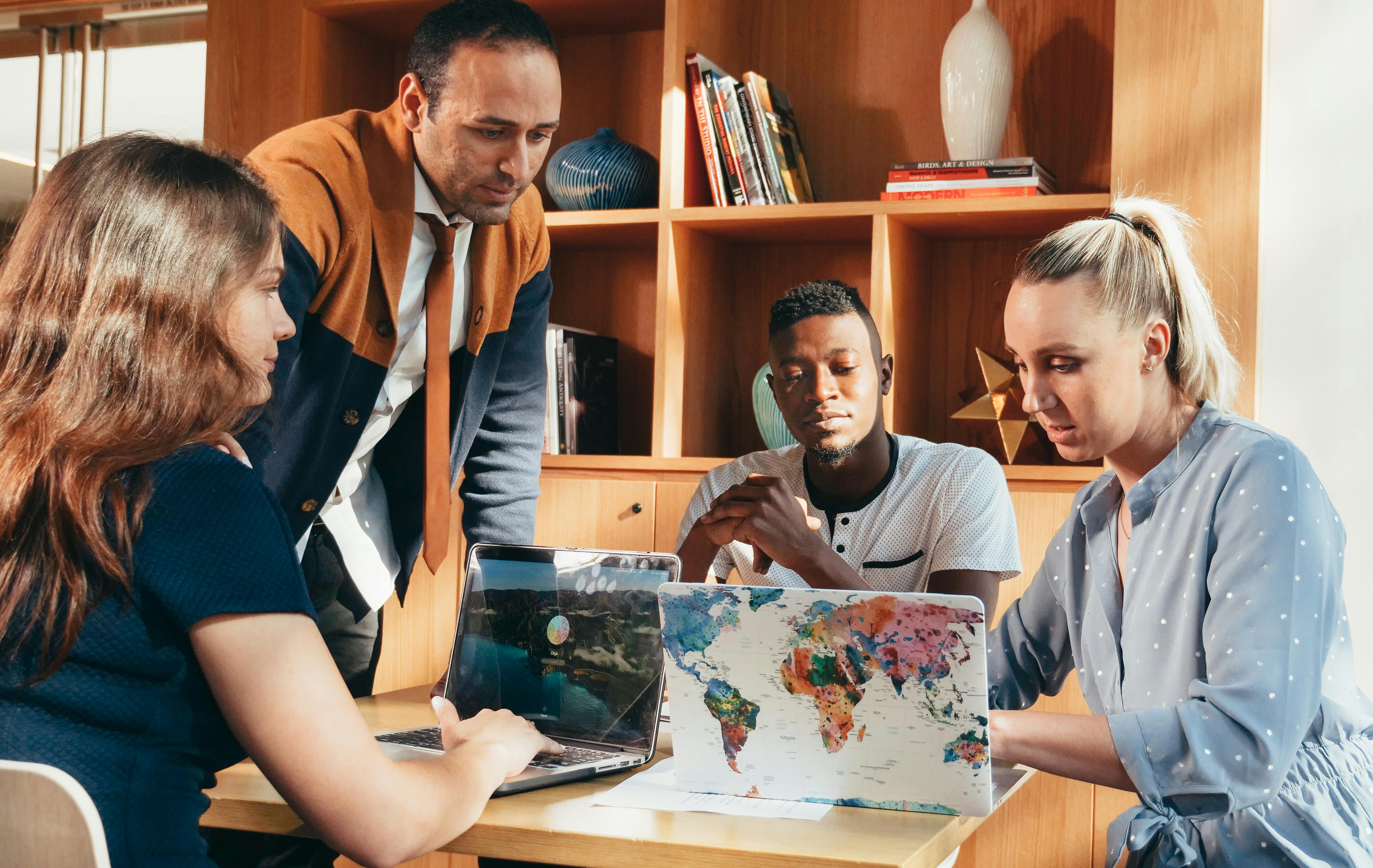 Young people working together on an assignment as teacher stands by