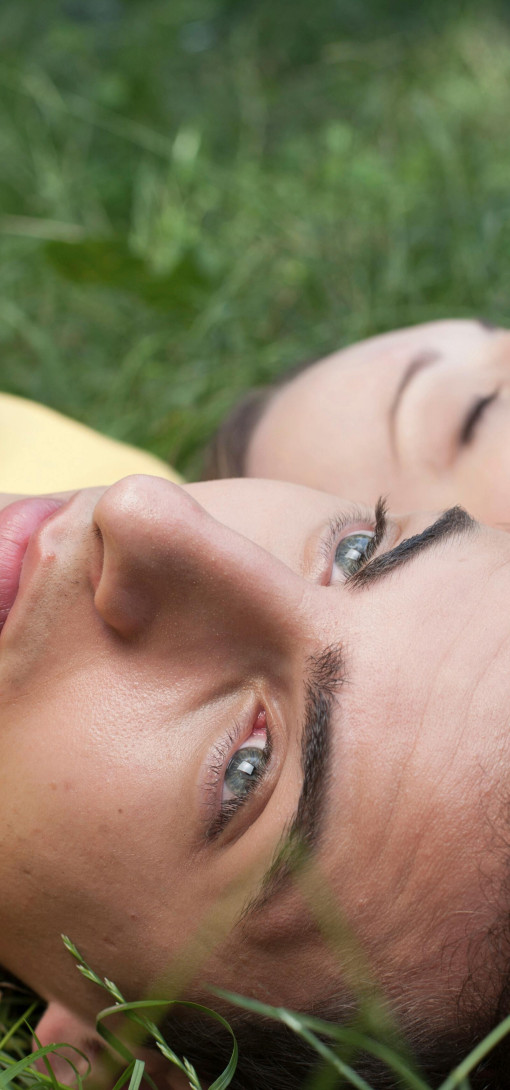A young man and woman lying in the grass, looking pensive