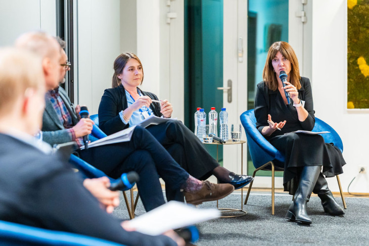woman with a microphone on a stage addressing another speaker