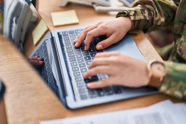 Hands on a laptop keyboard, person is wearing camouflage