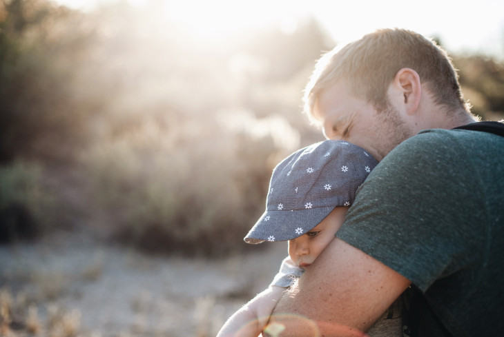 A father hugging a baby in the sunlight, to illustrate birth rates.
