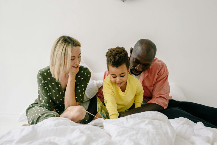 Parents and a child look at a book together, seeming relaxed