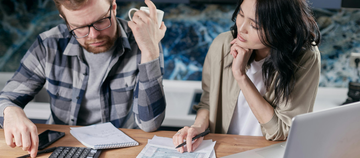 Two people, possibly a couple, looking worriedly at a calculator